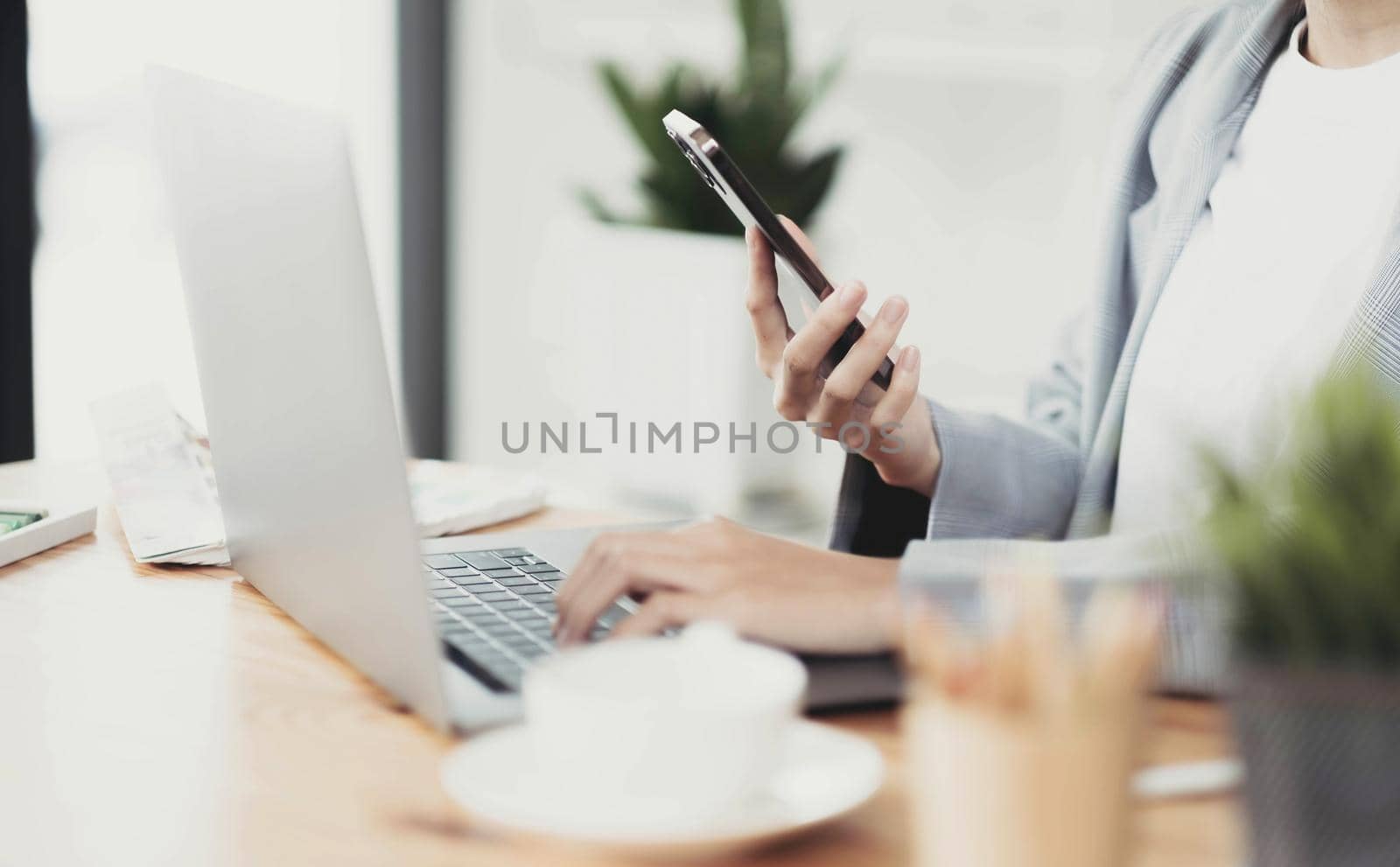 Cropped shot of businesswoman working with laptop computer and searching information smart phone at office desk. by wichayada