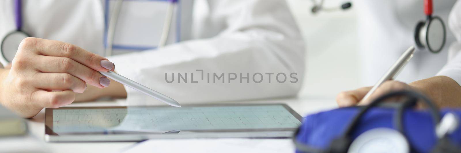 Close-up of female practitioner pointing with stylus on tablet screen. Woman cardiologist discussing cardiogram of patient with colleague. Modern medical technology and healthcare concept