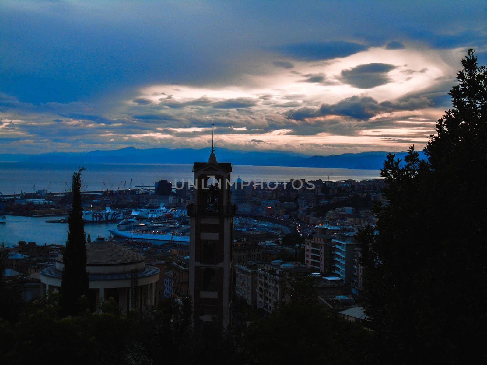 Genova, Italy - February 22, 2022: Evening view of Genoa (Genova) port, Italy with port cranes and industrial zone. Genoa, Italy. Lanterna lights by night. City illuminated behind the sea.