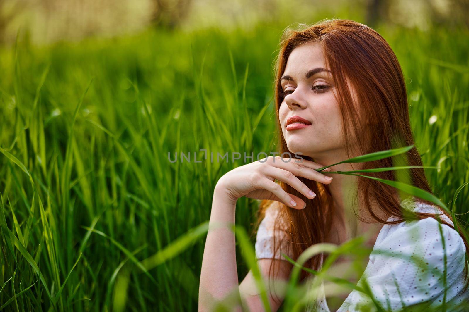 portrait of a blissfully smiling woman sitting in the grass with a leaf in her hand. High quality photo