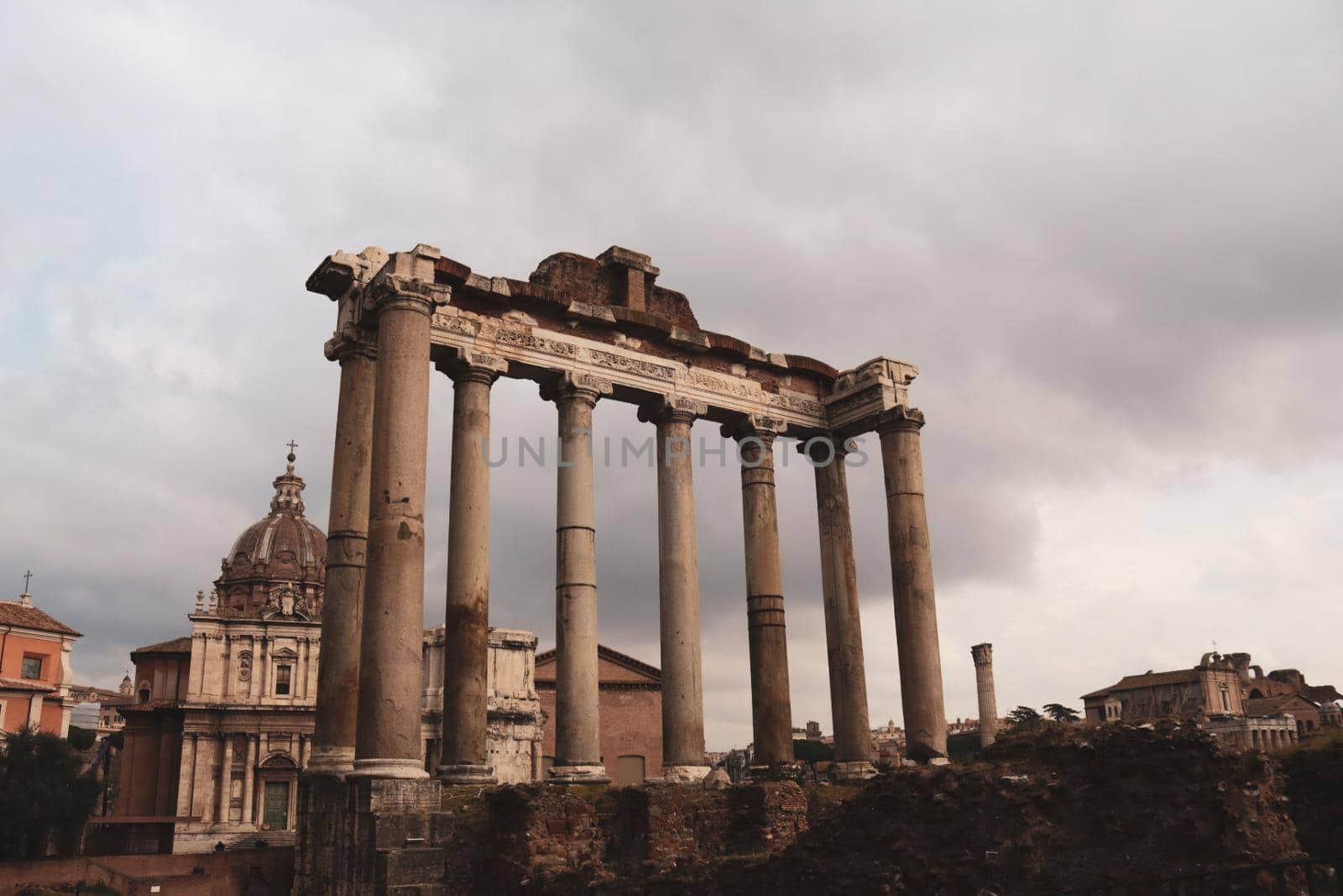 ROME, ITALY - February 05, 2022: Panoramic view around the Colosseum in city of Rome, Italy. Cold and gray sky in the background. Macro photography of the green parks with the old buildings.