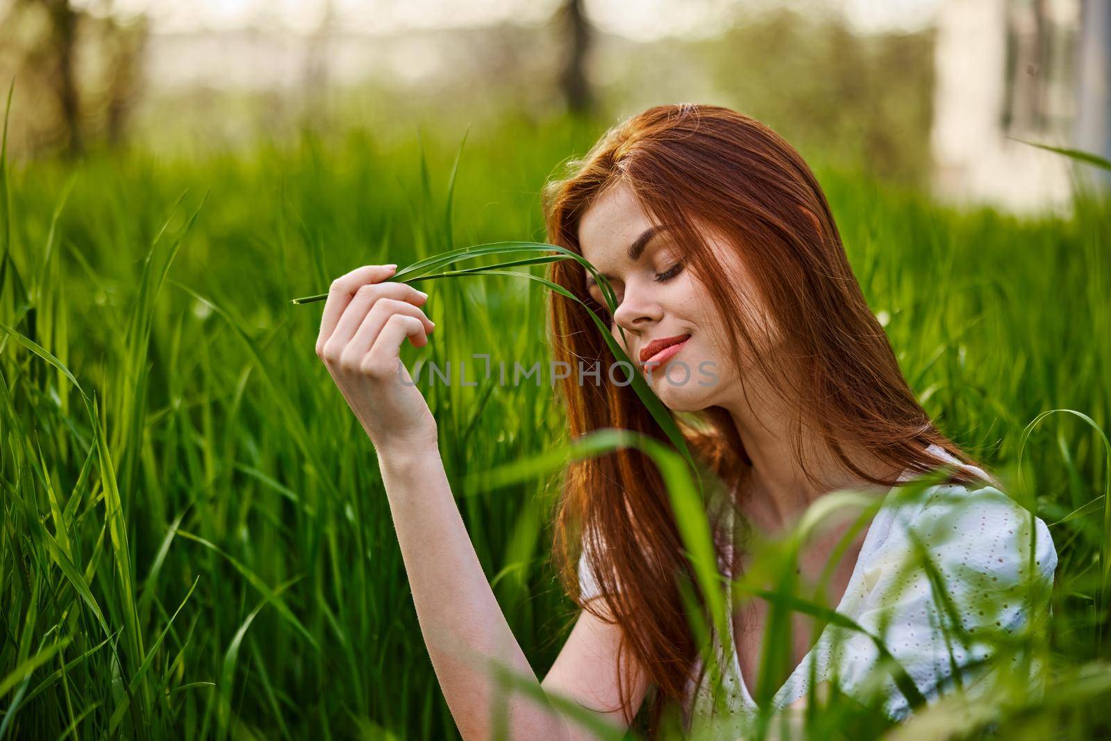 portrait of a cute red-haired woman sitting in tall grass and holding a leaf in her hands. High quality photo