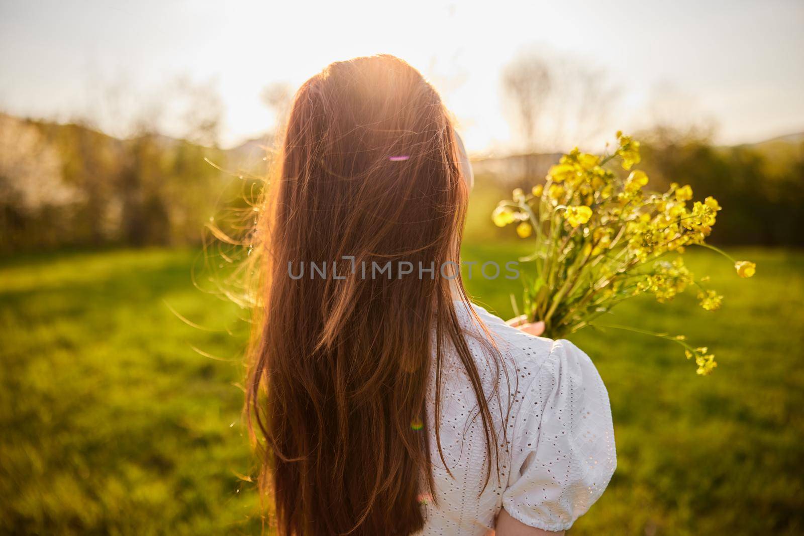 photo from the back of a red-haired woman with a bouquet of flowers in the rays of the setting sun. High quality photo