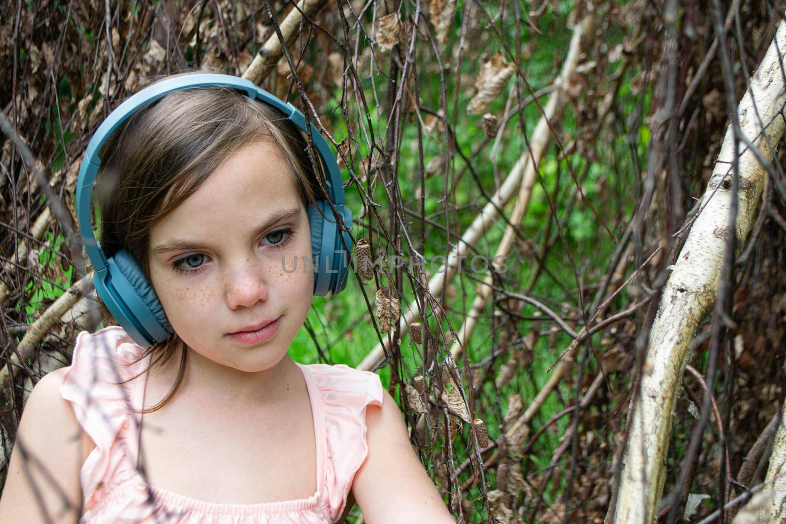 Young beautiful girl fooling around with a branch and wearing headphones on them to listen to music or block out sound due to auditory sensitivity. High quality photo