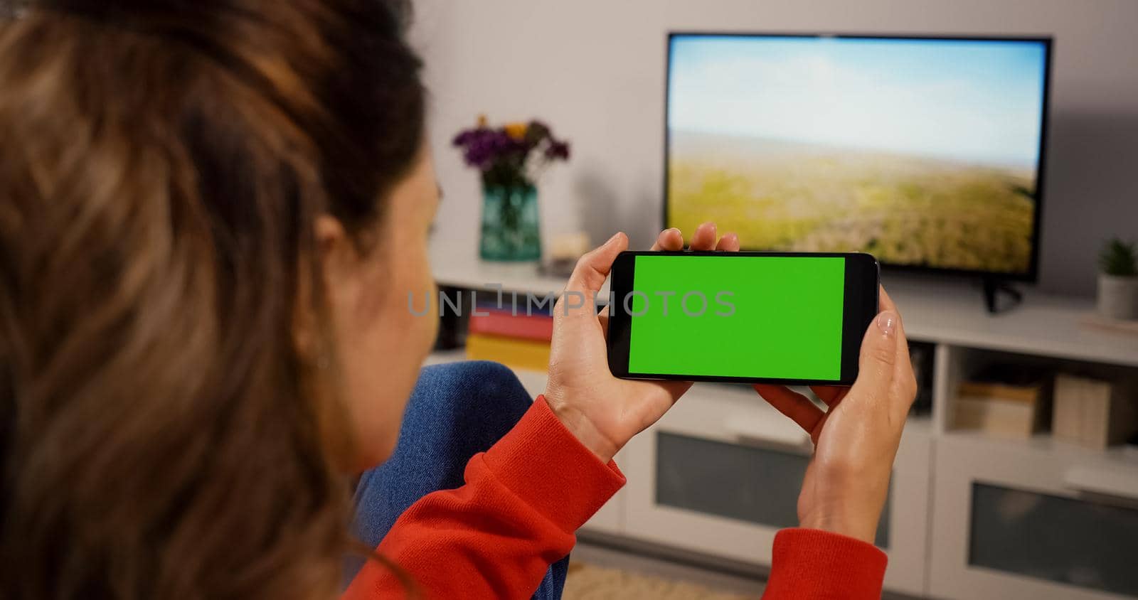 Phone Horizontal Green Screen for Copy Space Close up Chroma Key Mockup. Back over the shoulder view Girl watching video movie on couch Home. Hand phone holding technology users.