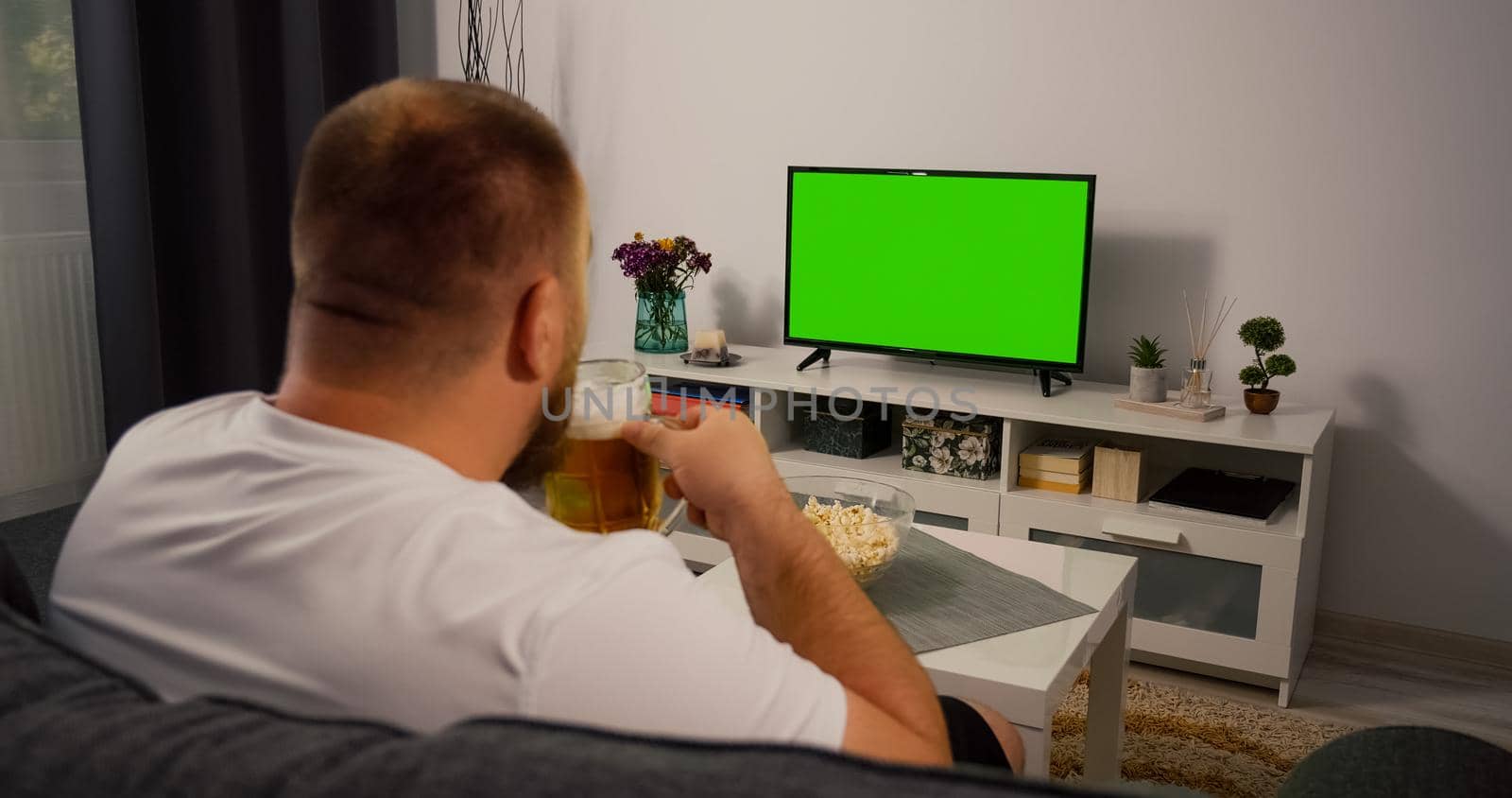 Man Watching Green Screen TV at home. Drink Beer Eating Popcorn. Over the Shoulder Back view. Chroma key.