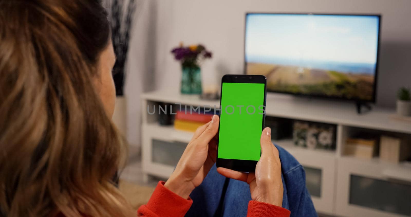 Woman at Home Sitting on a Couch using Smartphone with Green Mock-up Screen, Doing Swiping, Scrolling Gestures. Girl Using Mobile Phone, Internet Social Networks Browsing.