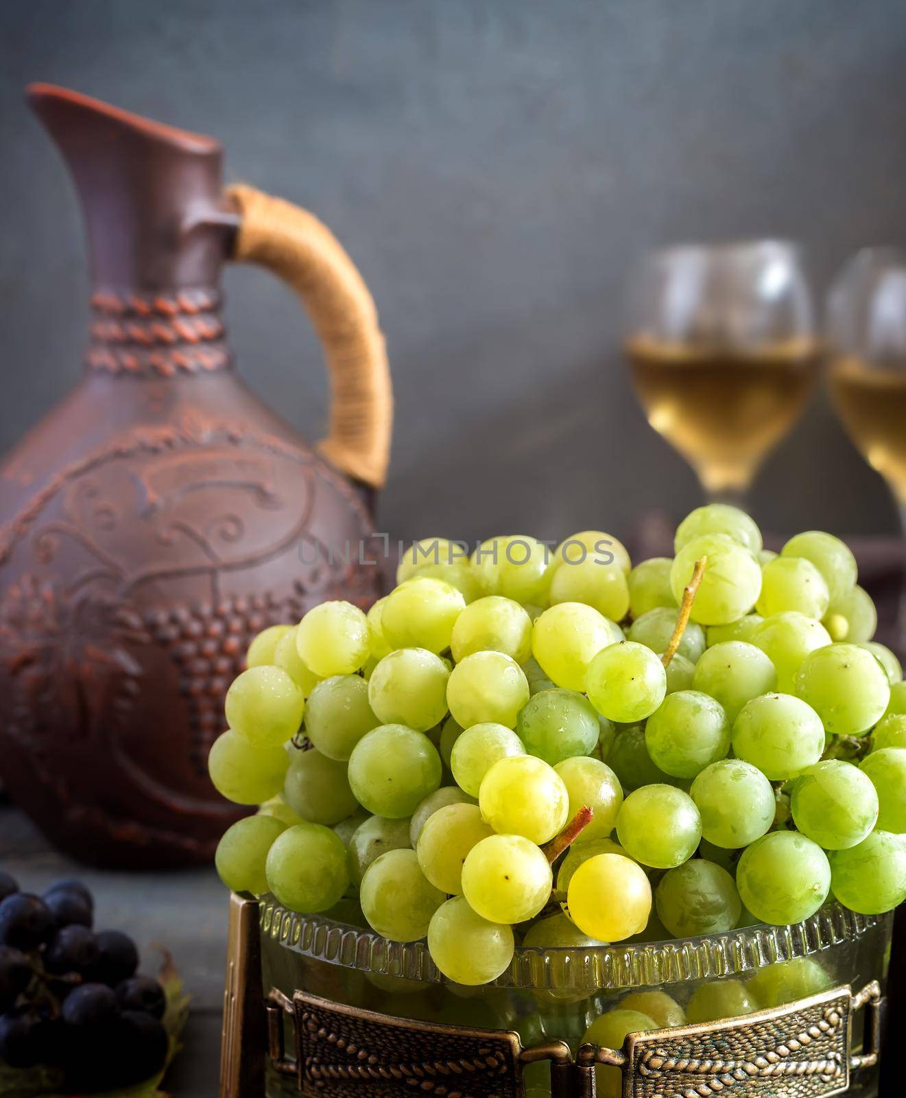 On the table in glass vase green grapes, near ceramic jug and two glasses guilt.