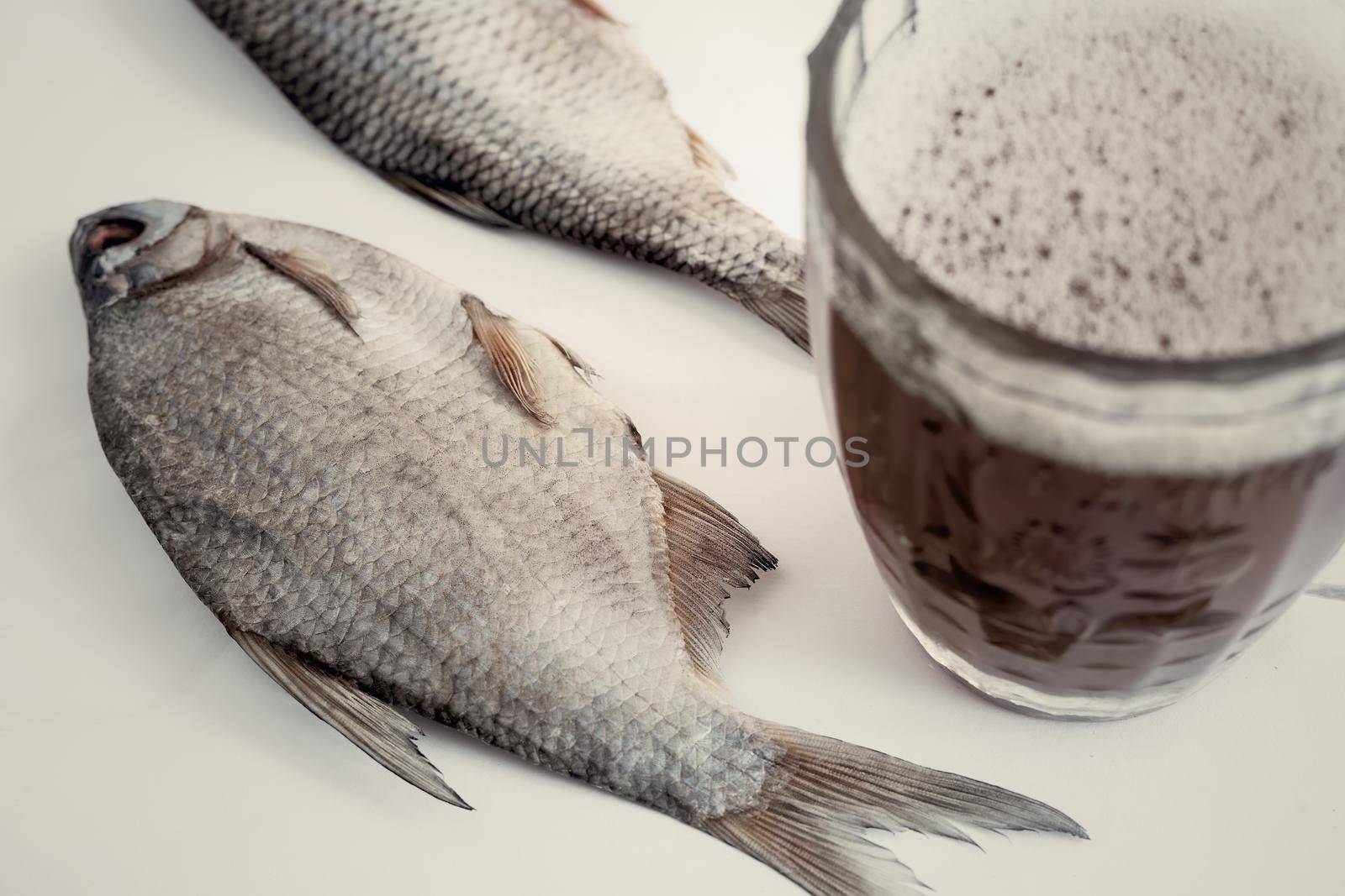 On the light surface of the table is dried fish, next to a glass of beer.