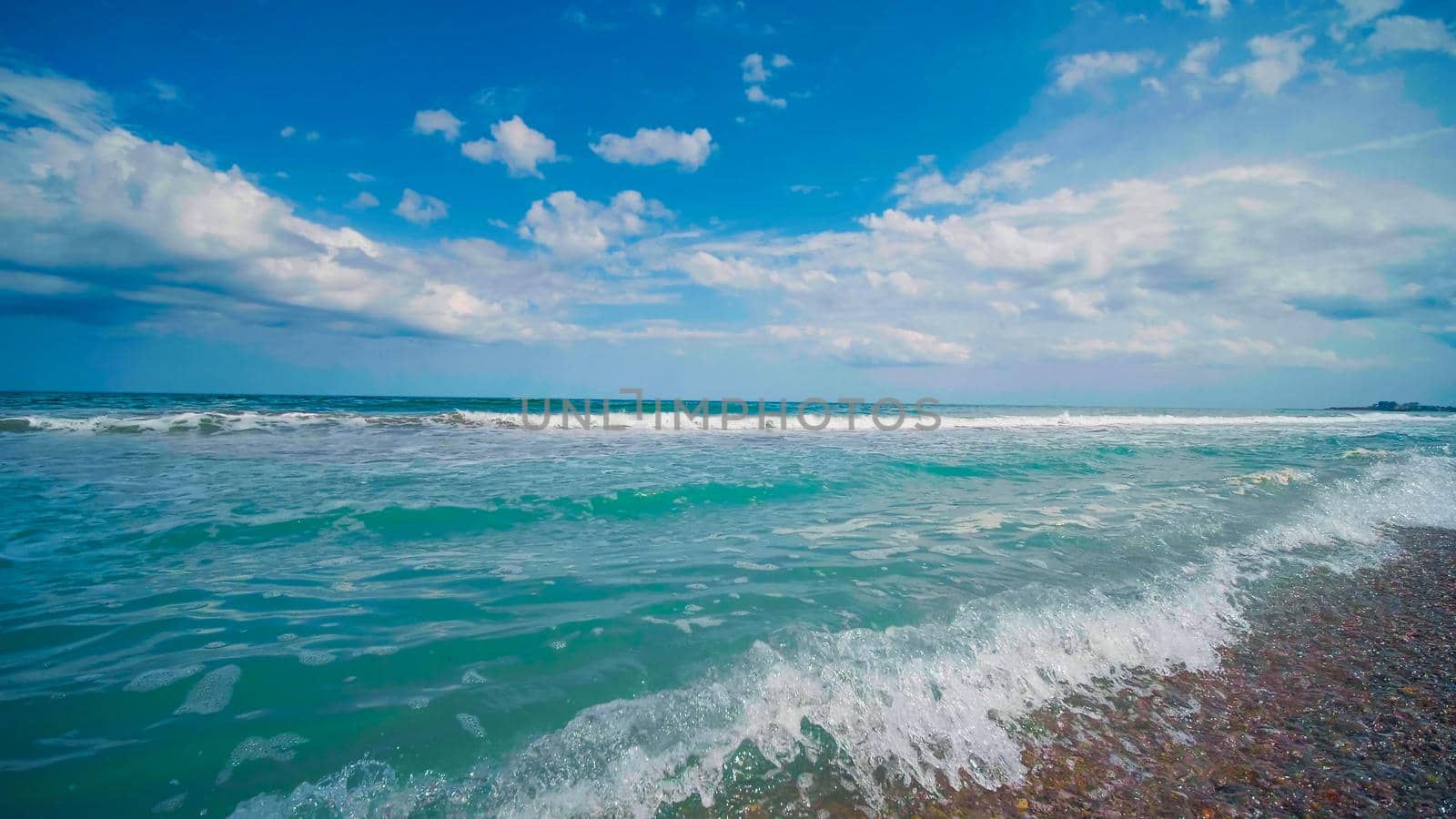 Beach sunny day, blue sky. Beautiful seascape. White foamywaves and white sand in the daytime. View of Black sea seachore.