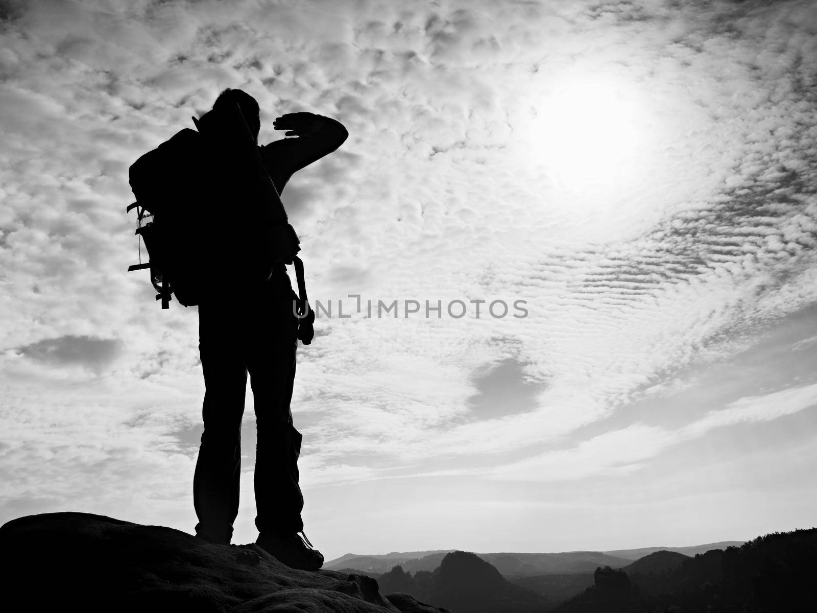 Tourist with big backpack stand on rocky view point and watching into deep misty valley bellow. Sunny spring daybreak in rocky mountains. by rdonar2