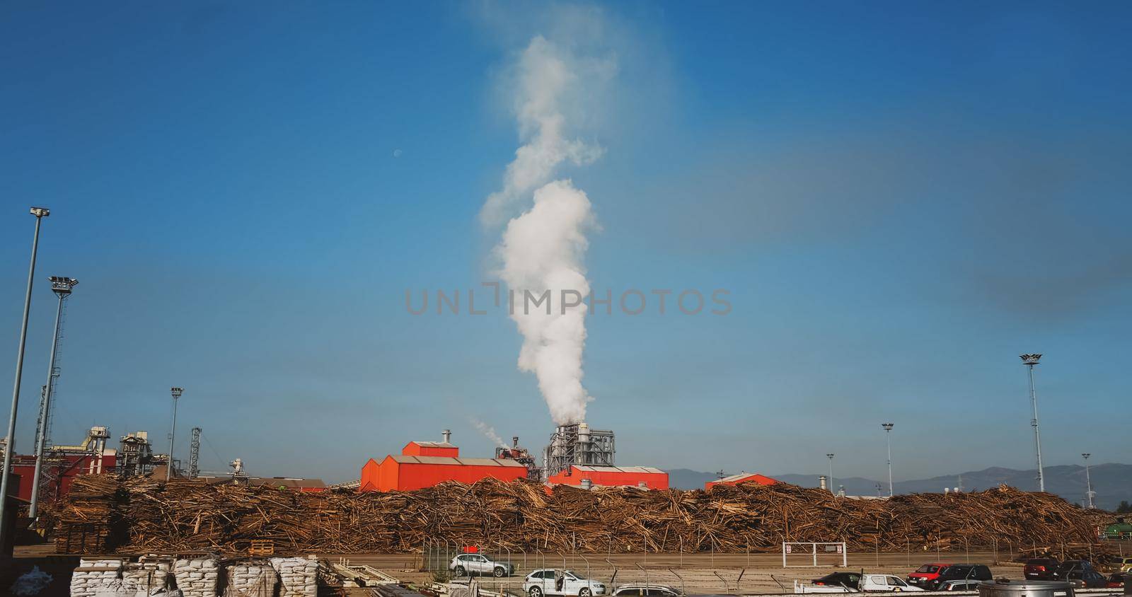 Air pollution of Furniture Factory. Smoke coming from the pipe. Wood raw material around factory. Industrial pollution.