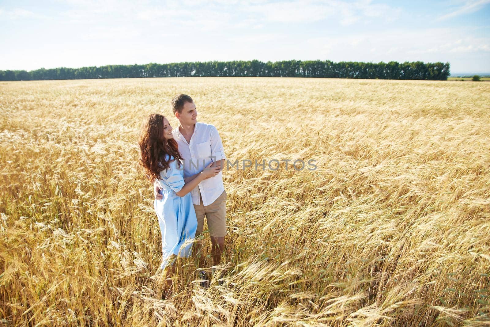 Smiling happy couple. Handsome Caucasian guy wearing white shirt gentle hugs a smiling girl with blond hair in dress
