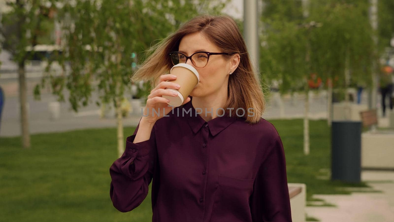 Young blonde Woman walking out of office building and drink coffee.