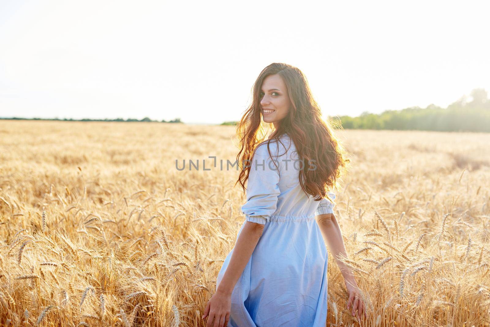 A young woman walks through a wheat field and looks at the camera