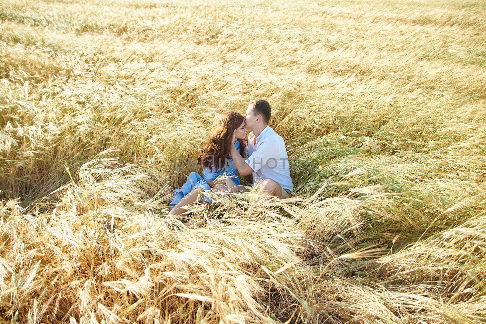 Lovely young couple kissing while sitting in a field. Love in the summer.