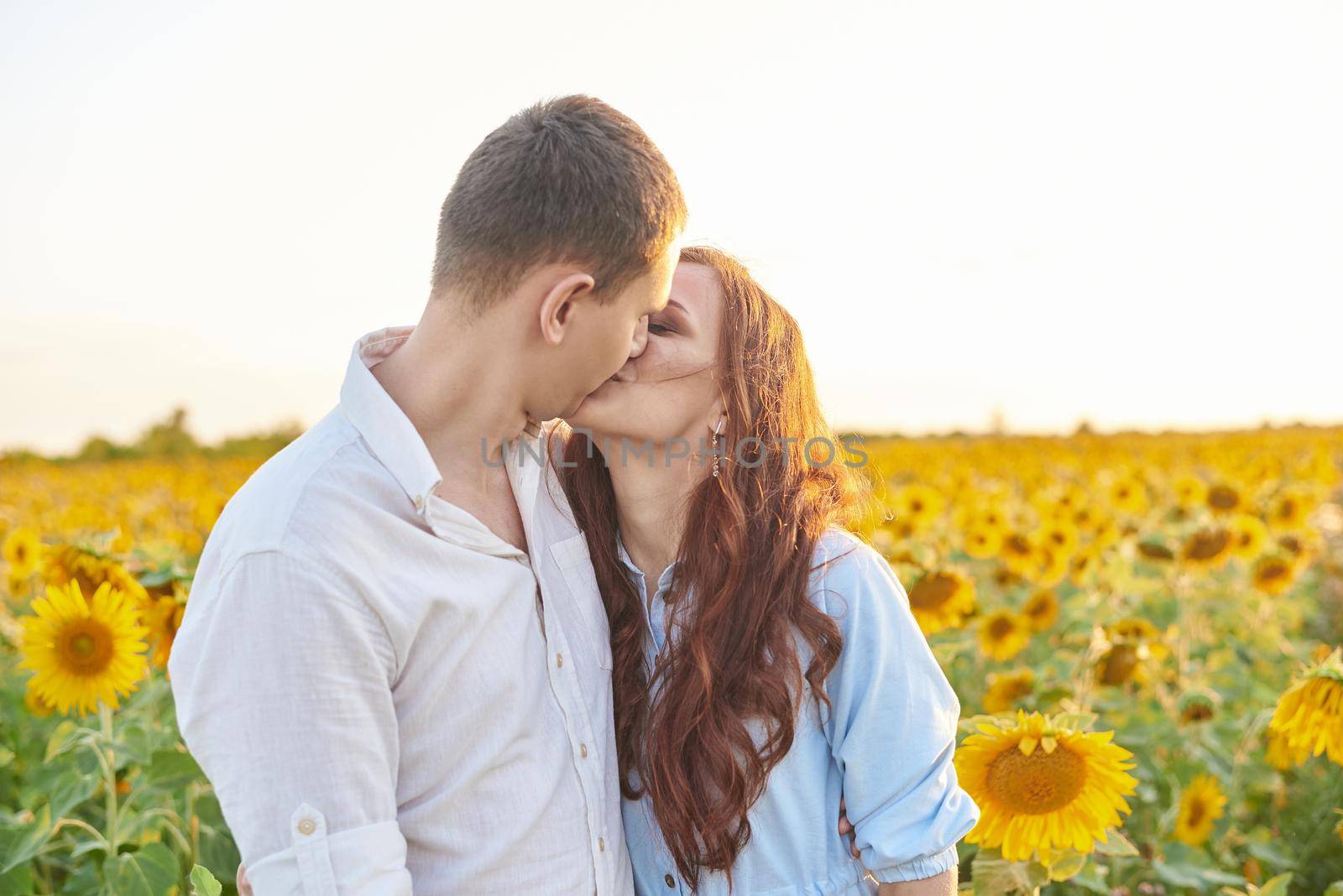 Kissing young couple portrait on sunflowers field. A love story.