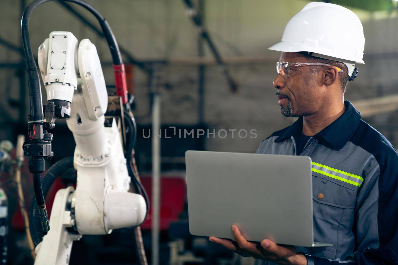 African American factory worker working with adept robotic arm in a workshop . Industry robot programming software for automated manufacturing technology .