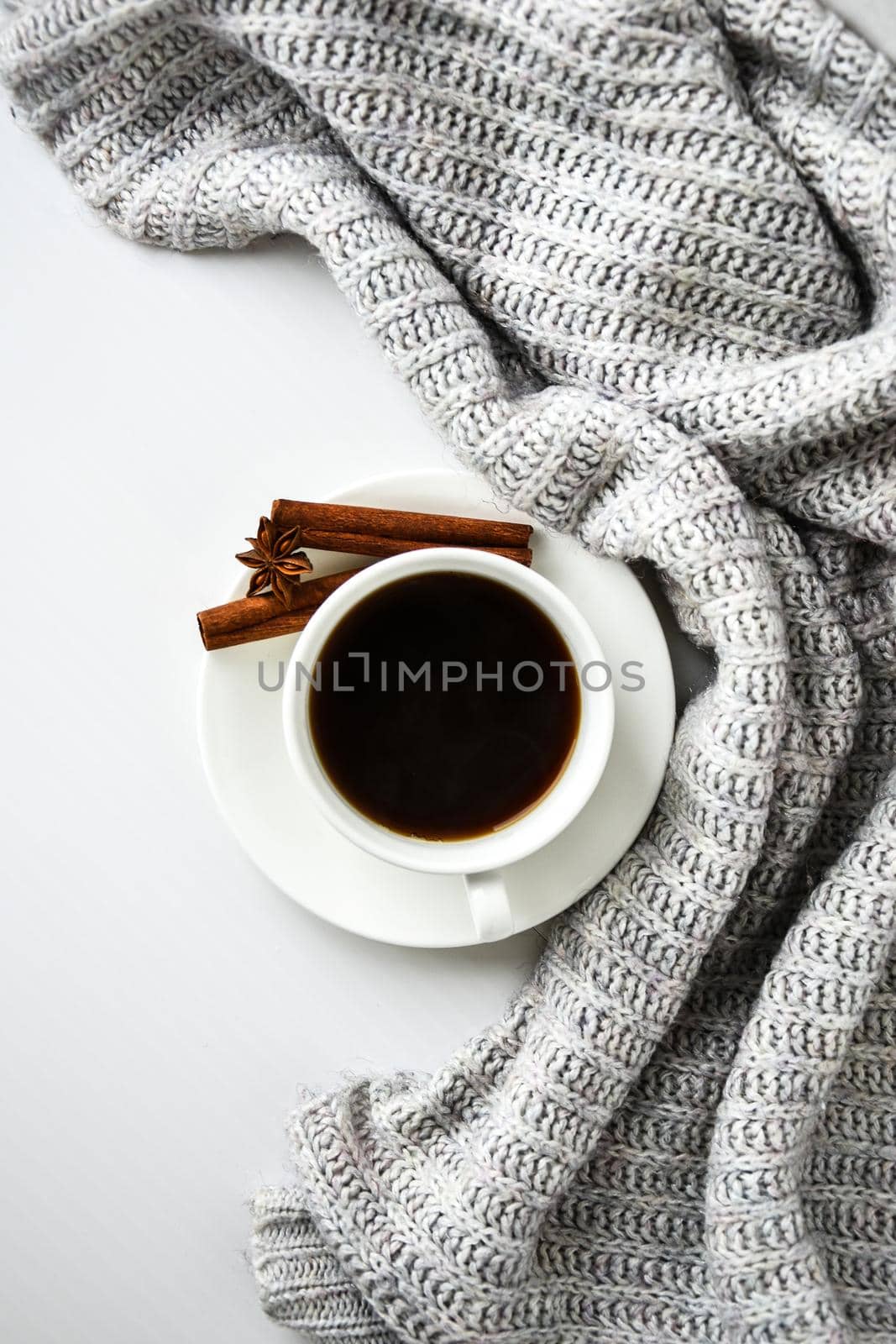 Cup of coffee with cinnamon sticks and anise star on white background. Sweater around. Winter morning routine. Coffee break. Copy space. Top view. Flat lay by anna_stasiia