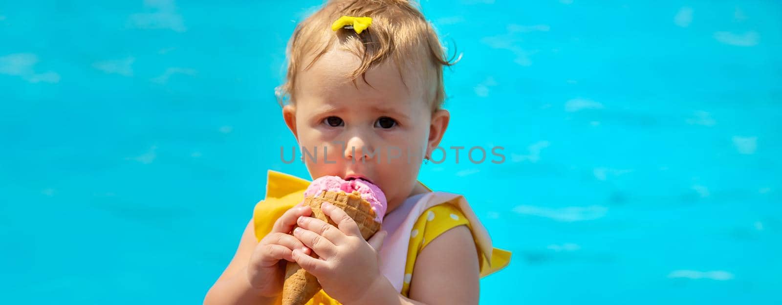 The child is eating ice cream near the pool. Selective focus. by yanadjana