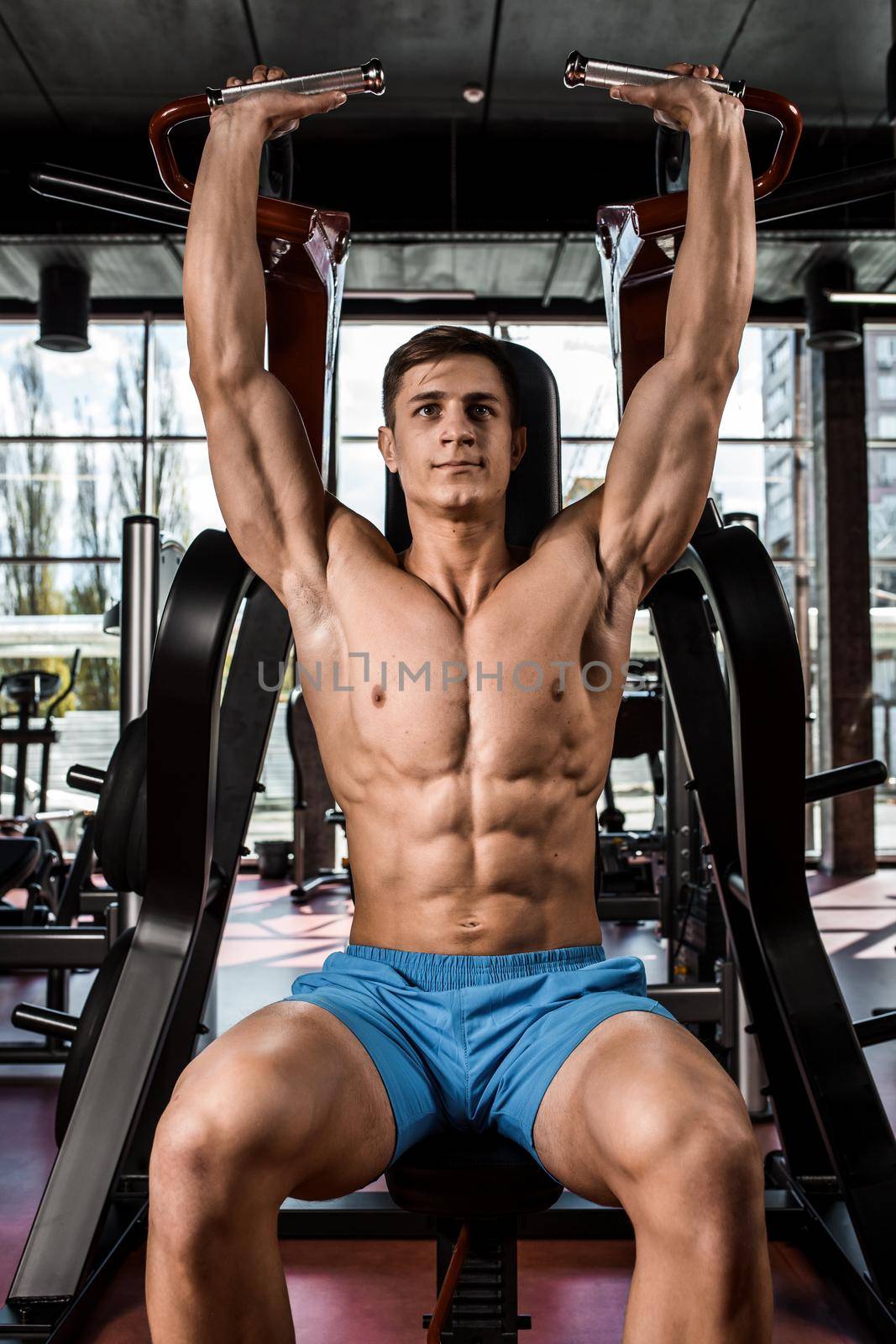 Tense muscles of hands under load. Man doing exercise for biceps in the gym. Work on tell muscles on the simulator. Photos for sporting magazines, posters and websites.