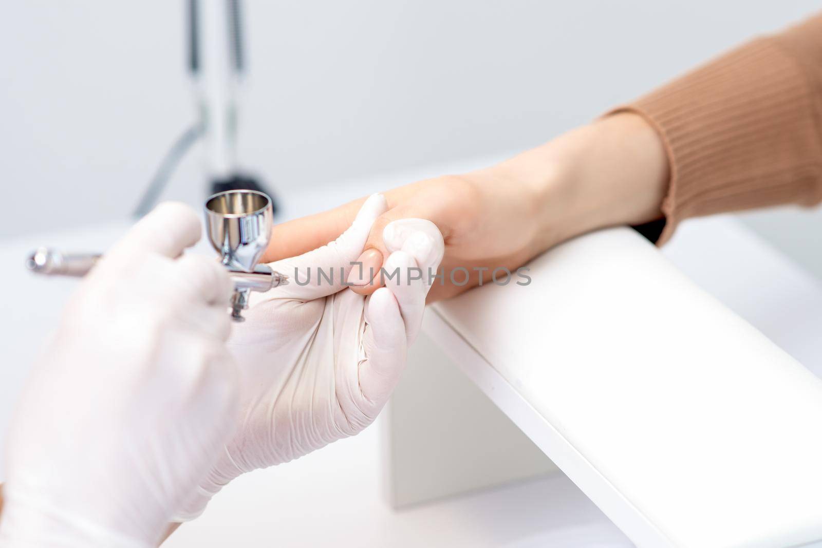 Young woman receiving manicure by airbrush in nail salon. Procedure for spraying paint on the nails