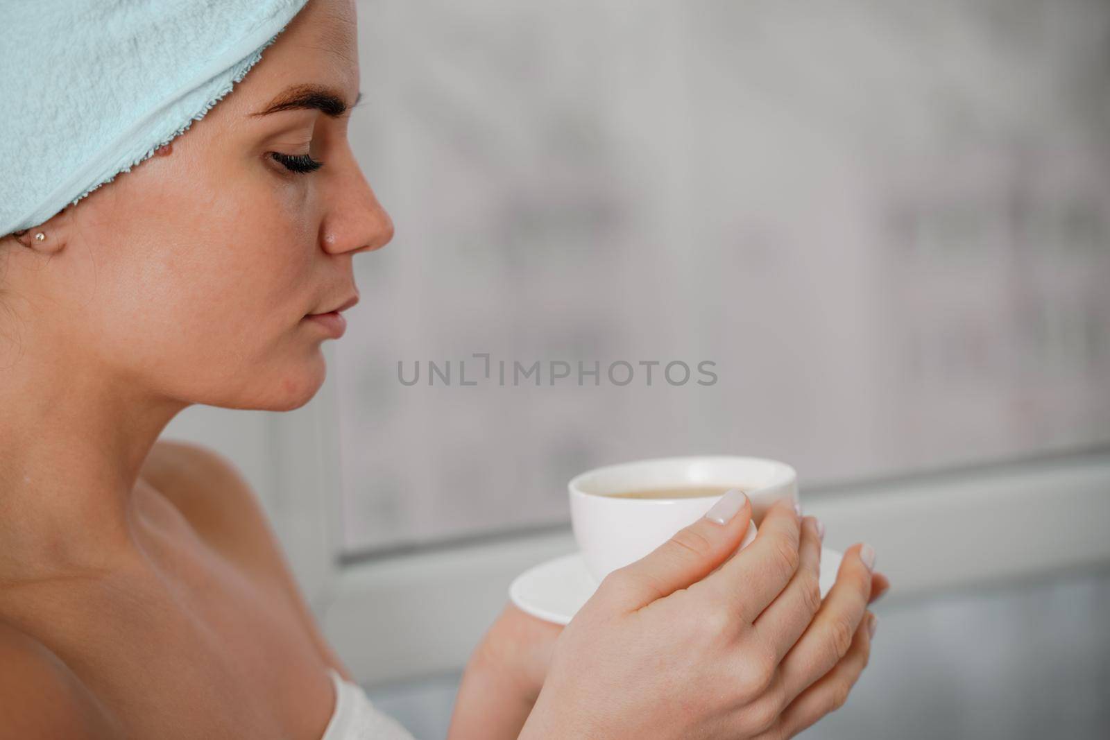 Young serene relaxed woman in spa bath towel drinking hot beverage tea coffee after taking shower bath at home. Beauty treatment, hydration concept