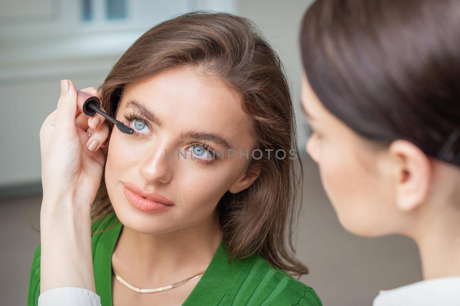 Professional makeup artist applying mascara on lashes of beautiful young caucasian woman in beauty salon