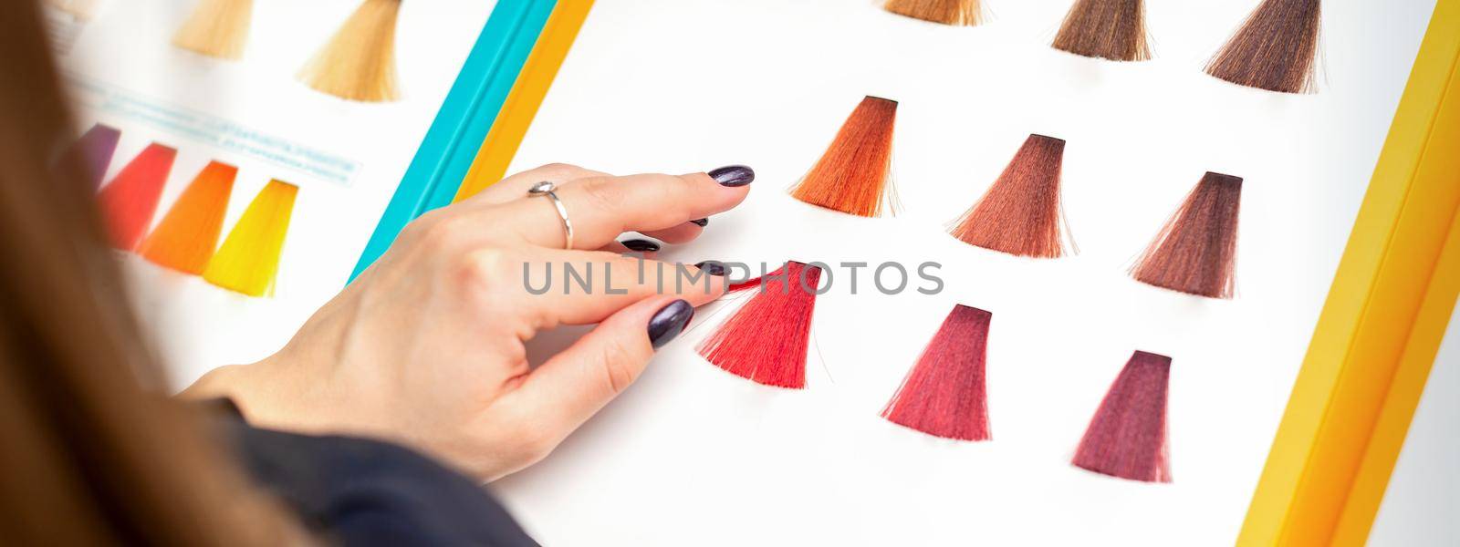 Customer's female hand choosing pink or red colour for hair colouring before hair dyeing in hair salon