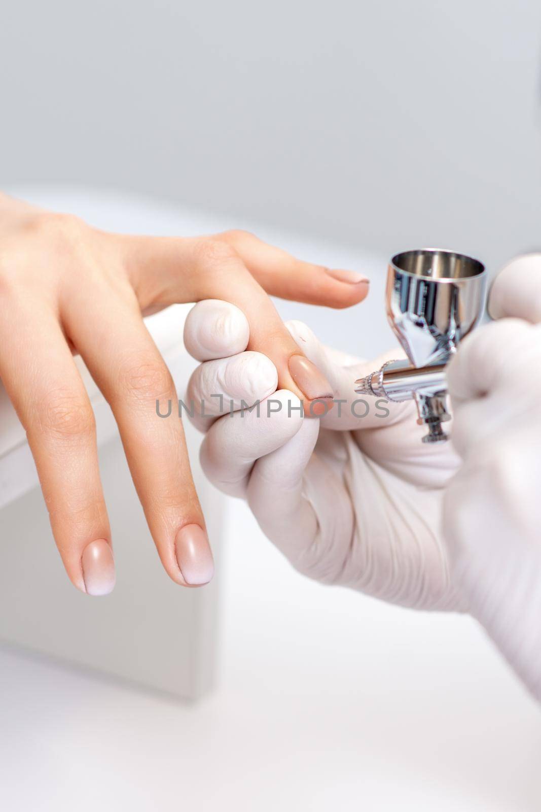 Young woman receiving manicure by airbrush in nail salon. Procedure for spraying paint on the nails