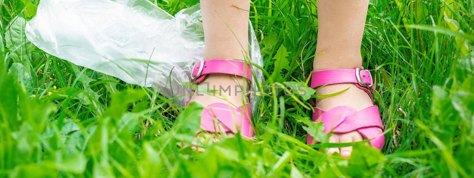 plastic bags trash with children's feet on green grass while cleaning the park from plastic debris