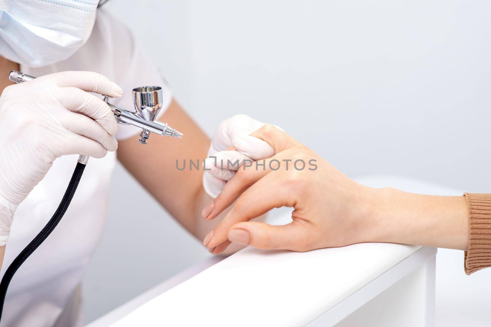 Young woman receiving manicure by airbrush in nail salon. Procedure for spraying paint on the nails