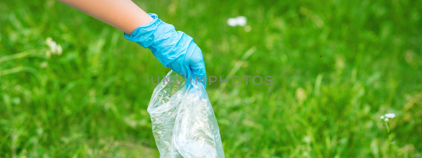 Hand of child cleans the park from plastic debris lying on the green grass