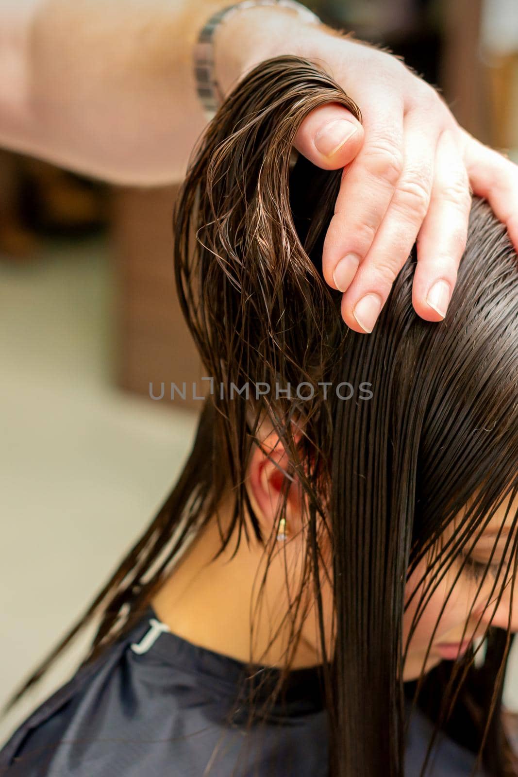 Young woman receiving treatment her hair by hands of professional hairdresser in hair salon