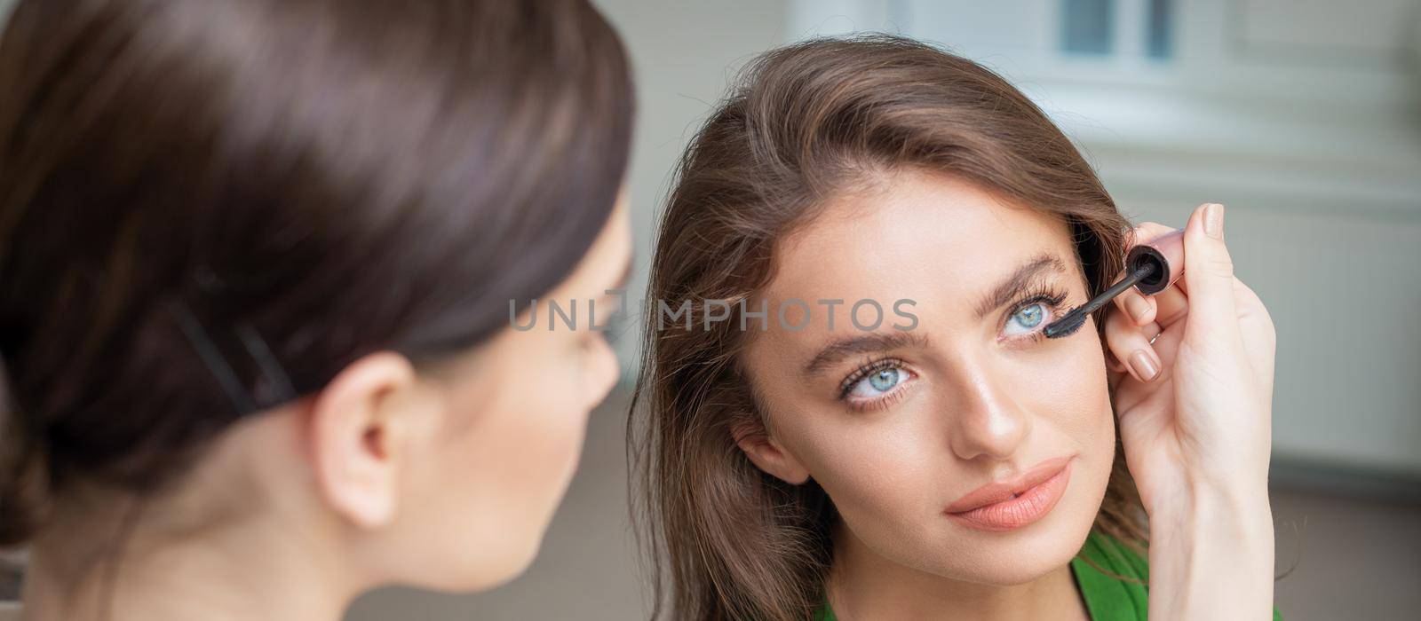 Professional makeup artist applying mascara on lashes of beautiful young caucasian woman in beauty salon