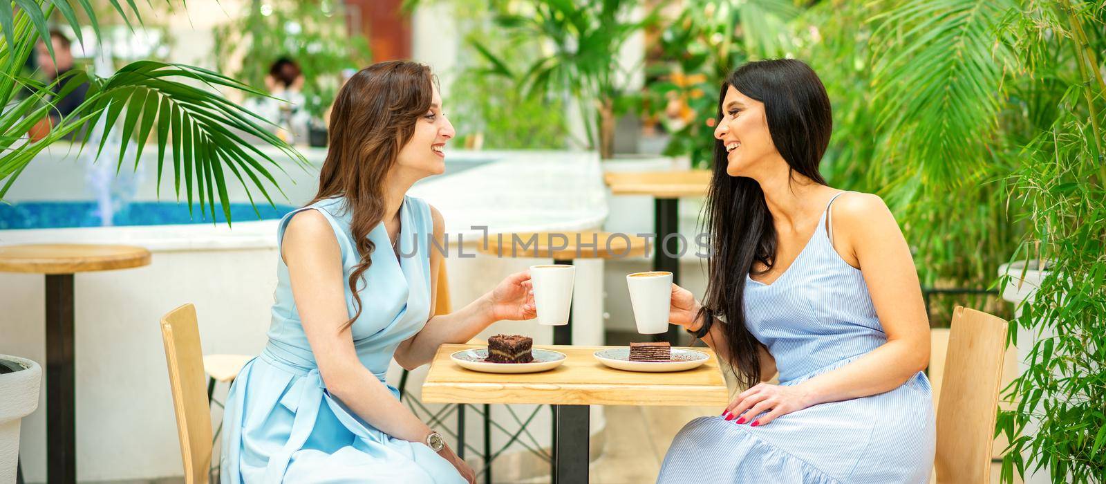 Two beautiful young caucasian smiling women with coffee cups at cafe outdoors