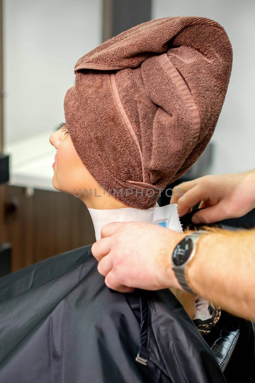 Hairdresser puts on black cape to female customer with towel on her head in hair salon