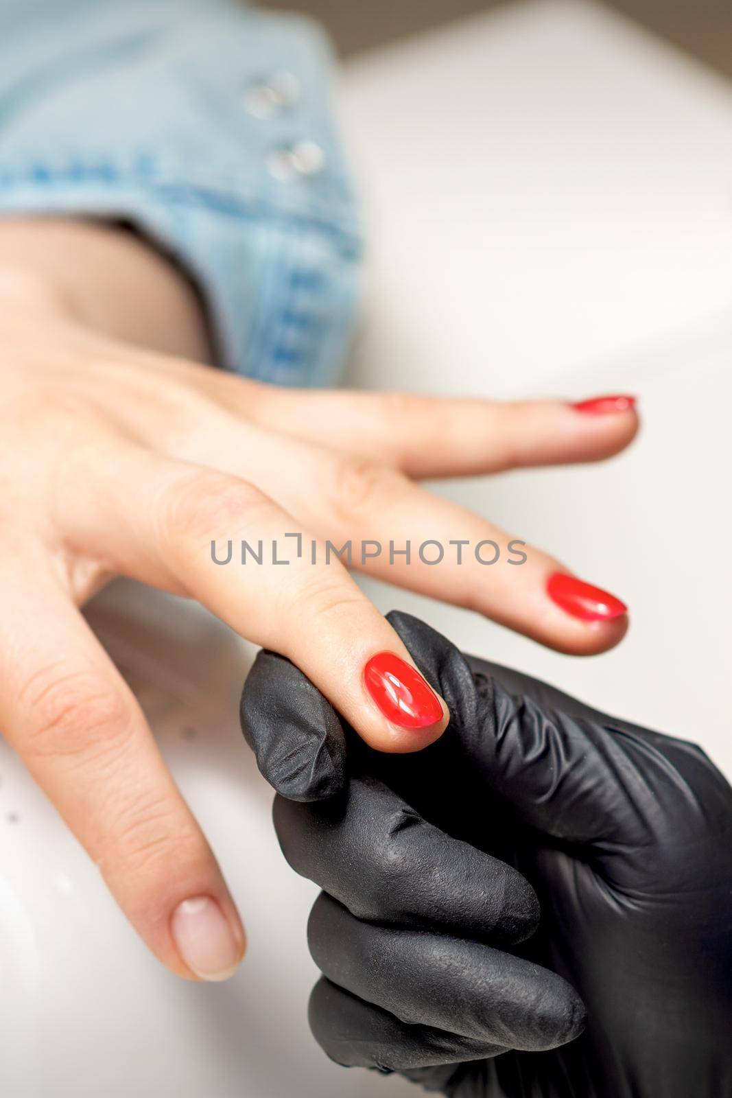 Young woman receives red nail polish by professional manicure master in nail salon