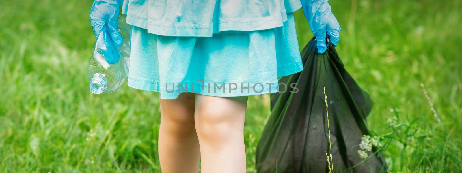 Little girl with crumpled plastic bottle and garbage bag in her hands while cleaning garbage in the park