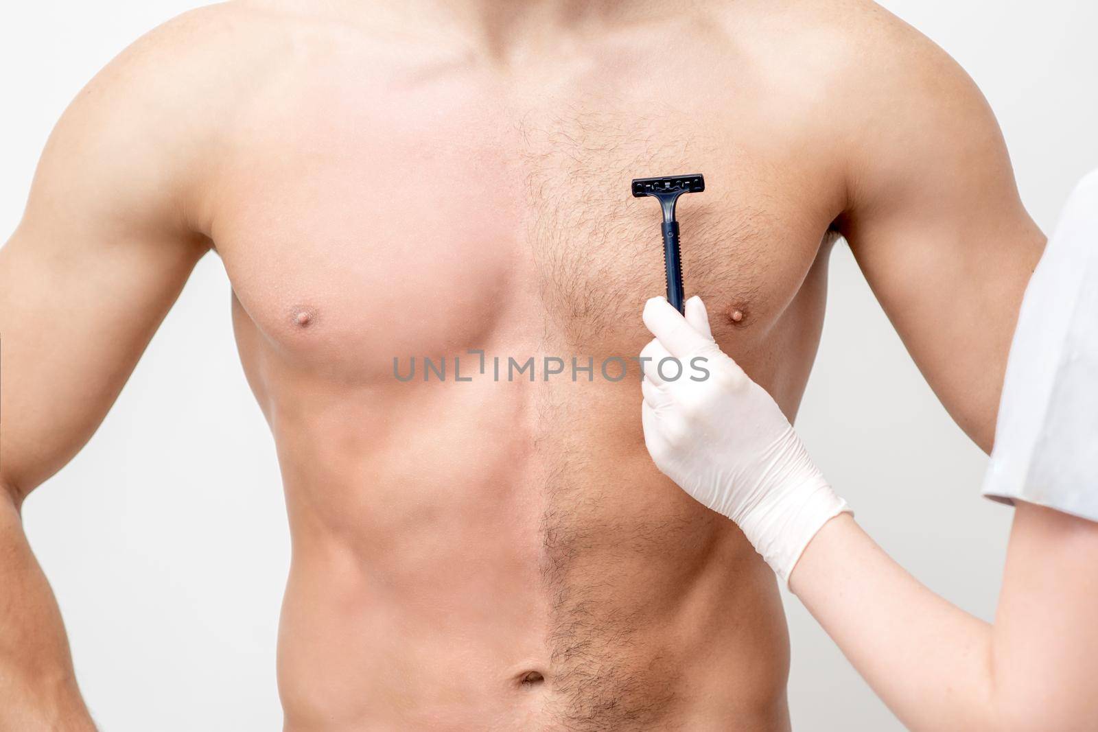 Hand of female beautician shaves chest of young man by razor. Concept of hair removal