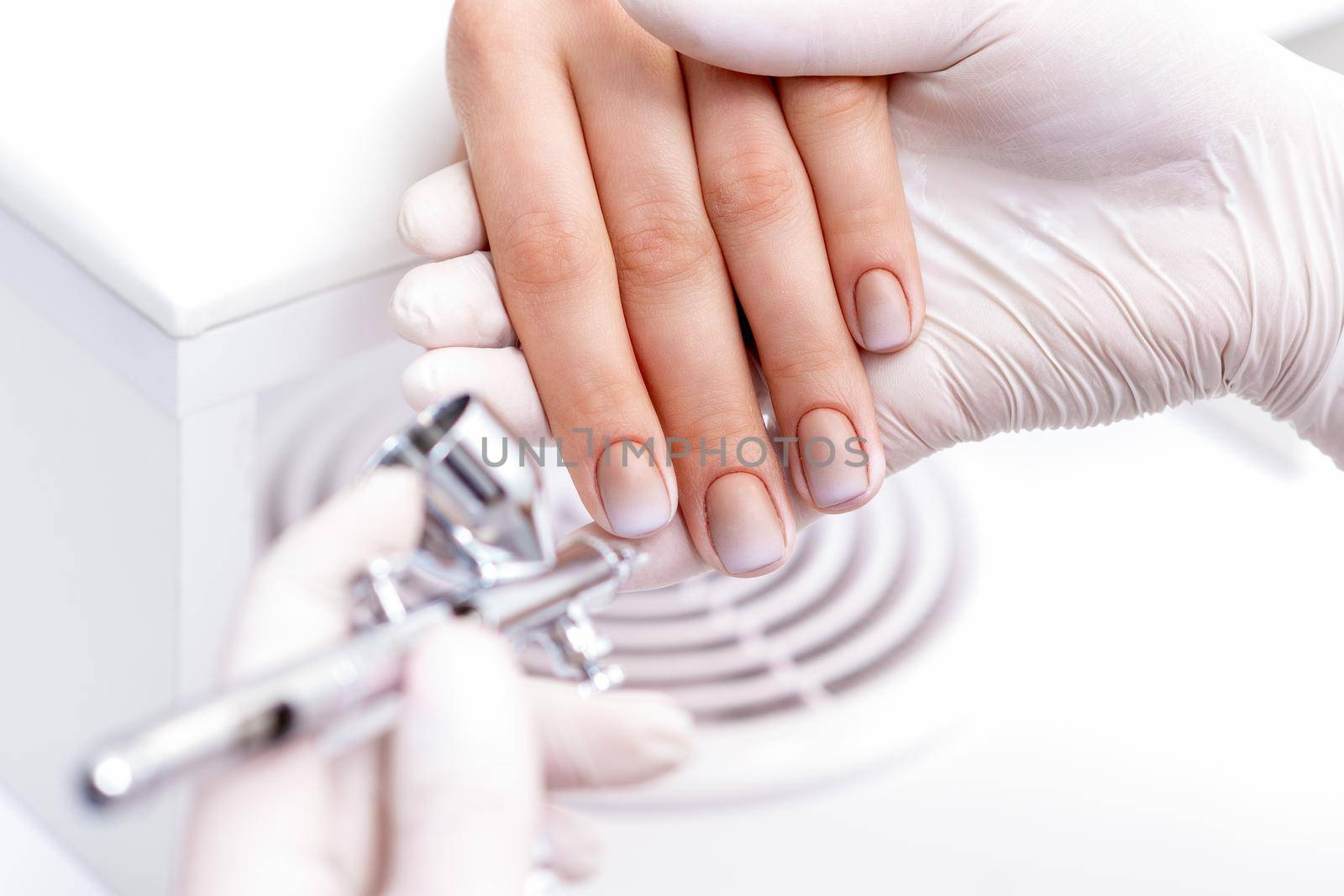 Young woman receiving manicure by airbrush in nail salon. Procedure for spraying paint on the nails