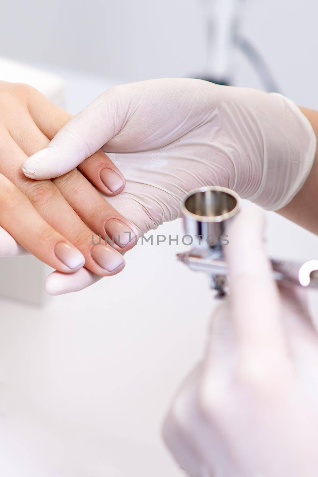 Young woman receiving manicure by airbrush in nail salon. Procedure for spraying paint on the nails