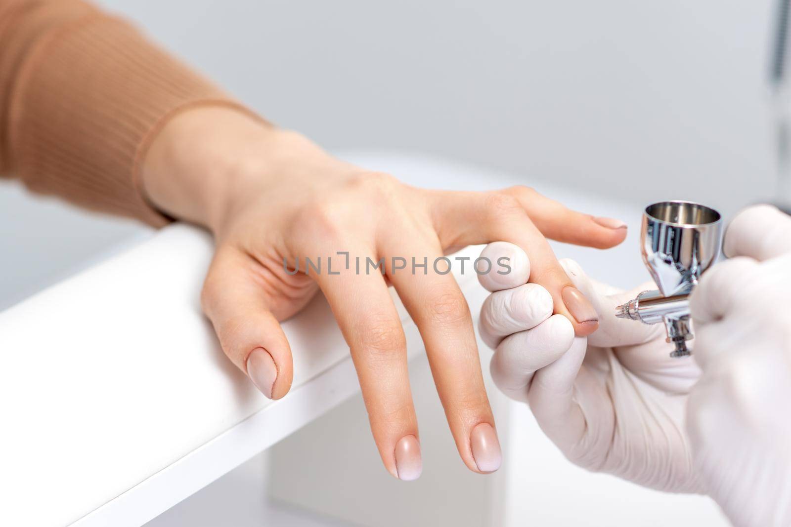 Young woman receiving manicure by airbrush in nail salon. Procedure for spraying paint on the nails