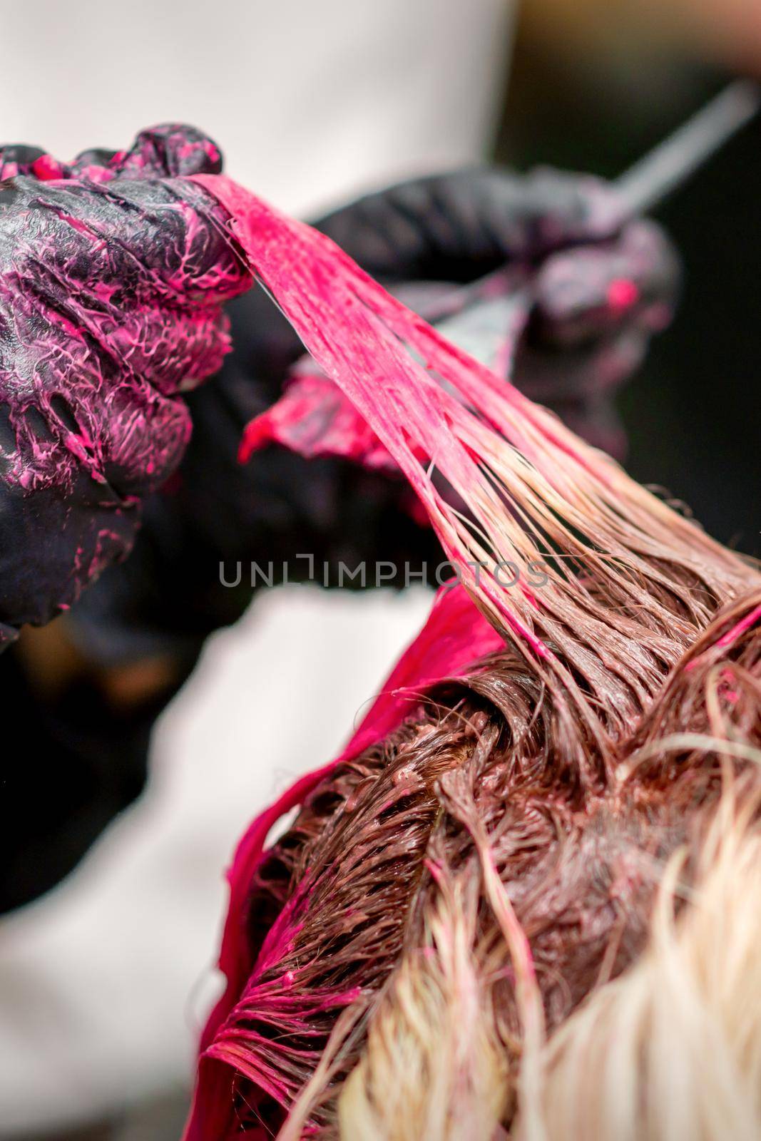 Close up shot of hair stylist dying hair of woman with pink dye in hair salon