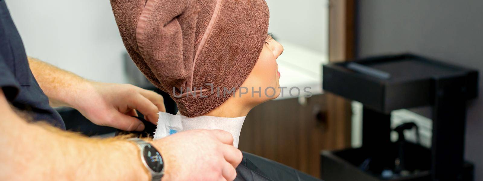 Hairdresser puts on black cape to female customer with towel on her head in hair salon