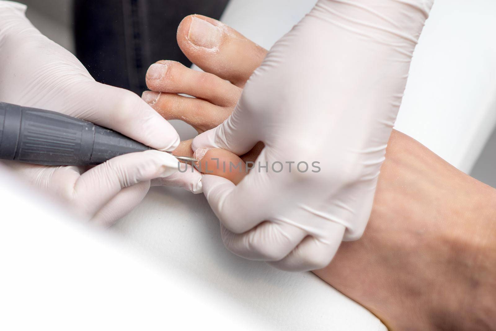 Process of professional pedicure. Pedicurist uses electric nail machine while doing pedicure on toes