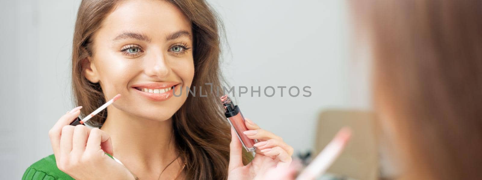 Beautiful young caucasian smiling woman applying gloss to the lips looking in the mirror