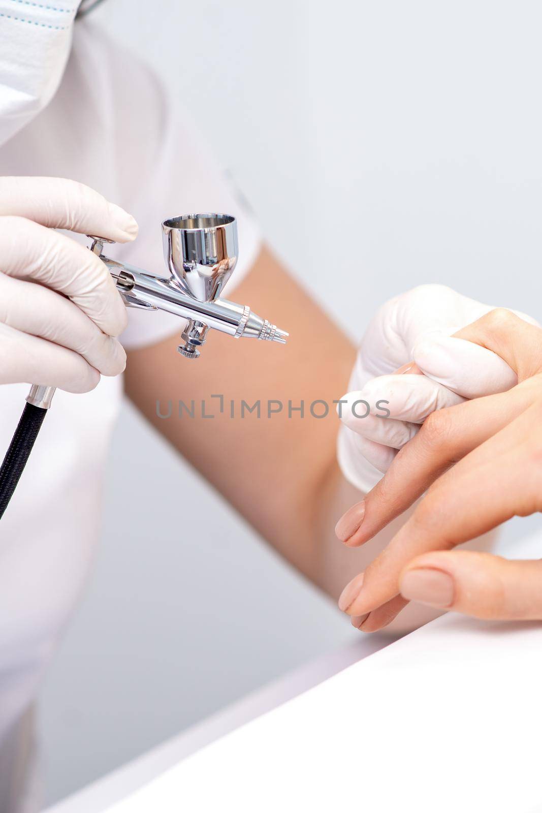 Young woman receiving manicure by airbrush in nail salon. Procedure for spraying paint on the nails