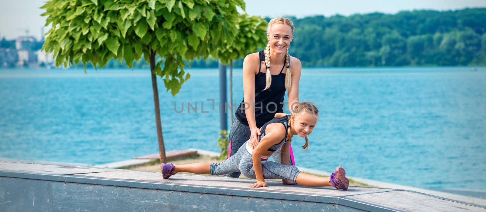 Mother and daughter doing gymnastic exercises on the mat at pier of river