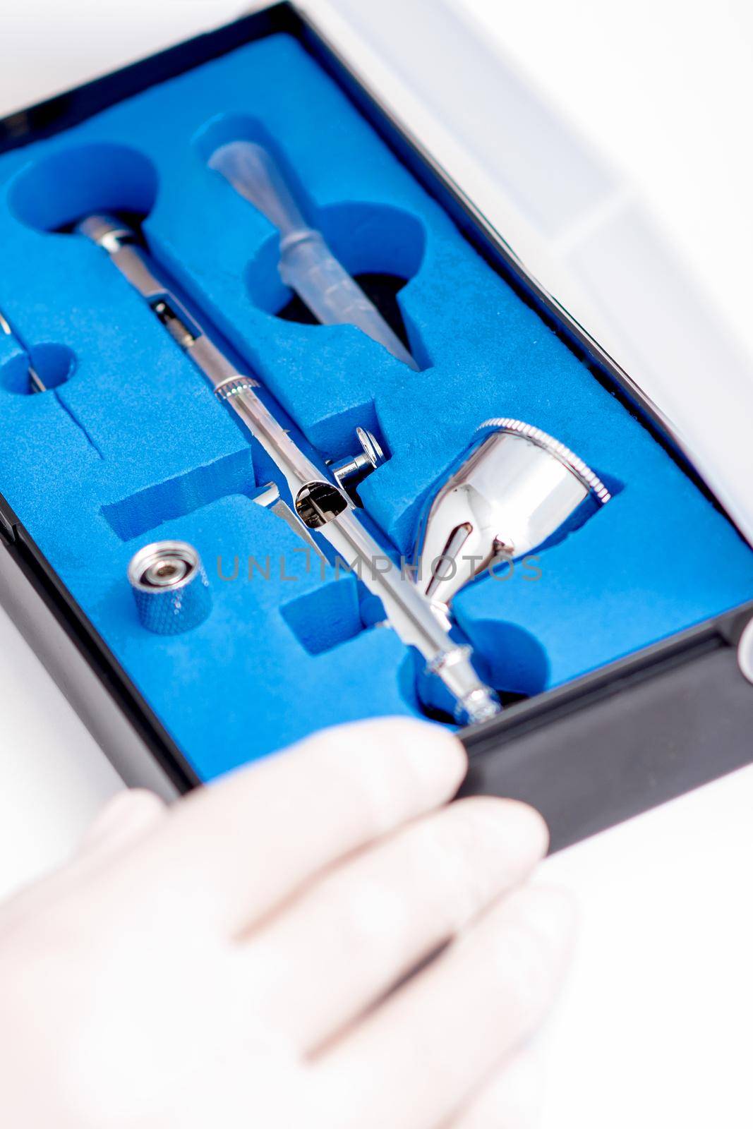 Close up shot of manicure master hand is taking out new clean airbrush tool for nails wearing gloves from the blue box